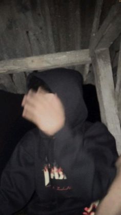 a man in a black hoodie is sitting under a wooden structure with his hand on the ground