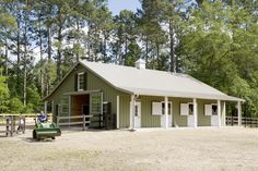 a small green building sitting in the middle of a field next to a fence and trees