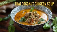 thai coconut chicken soup in a blue and white bowl on a wooden table with green leaves