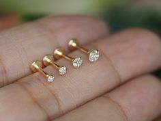 three small gold nose studs with diamonds on each one side, in the palm of someone's hand