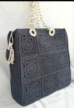 a black crocheted purse with tassels and chains hanging from the handle