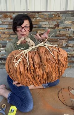 a woman sitting on the ground holding up a large pumpkin shaped like a human head