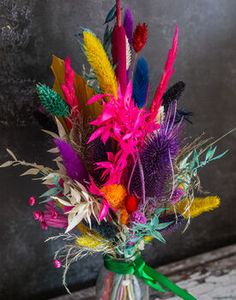 a vase filled with lots of different colored feathers on top of a wooden table next to a wall