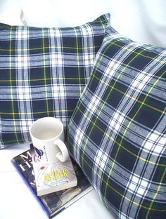 a plaid pillow with a book and coffee mug on it, next to a pair of pillows