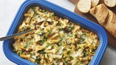 a blue casserole dish filled with pasta and spinach next to sliced bread