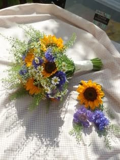 a bouquet of sunflowers and daisies on a white table cloth with other flowers