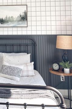 a bed with white and gray sheets in a bedroom next to a table with a clock on it