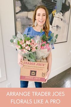 a woman holding a box full of flowers with the words arrange trader joe's florals like a pro