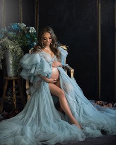 a pregnant woman sitting in a chair with her legs crossed and wearing a blue dress