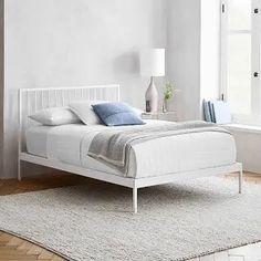 a white bed sitting in a bedroom on top of a wooden floor next to a window