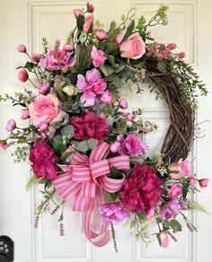 a wreath with pink flowers and greenery hanging on a door