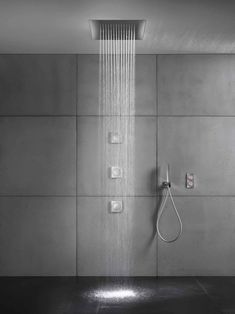 a shower head with water coming out of it in a tiled bathroom area, surrounded by grey walls