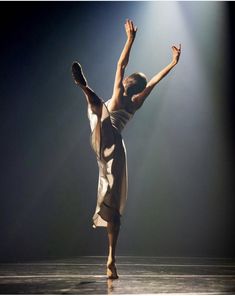 a woman is dancing on stage with her arms in the air while wearing a dress