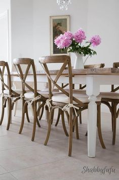 a dining room table and chairs with pink flowers in a vase on the top one