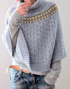 a woman wearing a sweater and jeans is holding her finger in her mouth while standing against a white wall