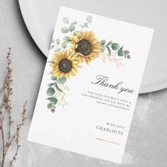 a thank card with sunflowers and greenery on the front, next to a plate