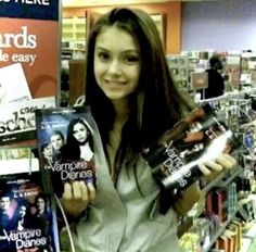 a woman holding two dvds in her hands and smiling at the camera while standing in front of a book store