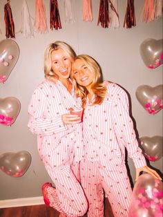 two women in pajamas hugging each other with balloons and tassels on the wall behind them