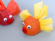 two fish made out of construction paper sitting next to each other on a gray surface