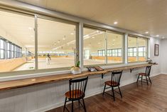 an empty room with several chairs and tables in front of large windows that look out onto a tennis court