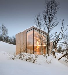 a small house in the middle of a snowy field with trees and bushes around it