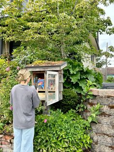 a woman standing in front of a wooden outhouse with plants growing on the roof