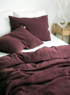 an unmade bed with maroon linens and pillows