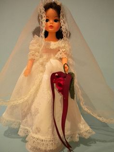 a doll dressed in a wedding dress and veil with a red ribbon attached to it