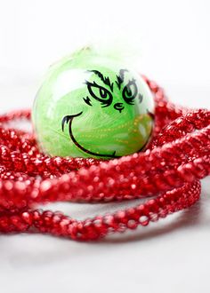 a green ball with a grin face drawn on it is surrounded by red bead