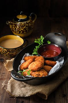 some food is in a black bowl on a wooden table next to cups and sauces