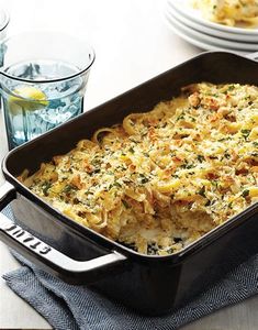 a casserole dish filled with pasta and cheese on a table next to water