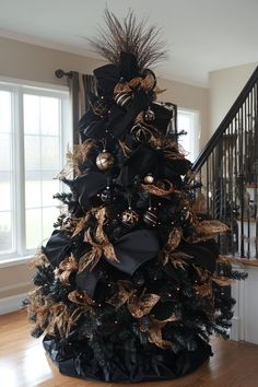 a black christmas tree with gold ornaments and bows on it's top is in the middle of a wooden floor