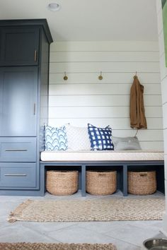 a bench with baskets underneath it in front of a blue cabinet and white shiplap wall