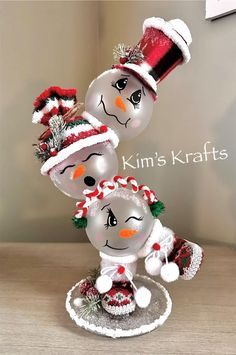 three glass snowmen with hats and scarves on their heads, one wearing a santa hat