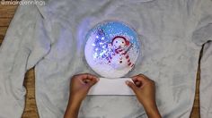 someone is painting a snowman on a white shirt with blue and red glitters