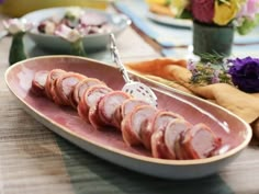 a platter filled with sliced meat on top of a wooden table next to flowers