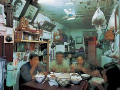 a group of people sitting at a table eating food in a room with pictures on the walls