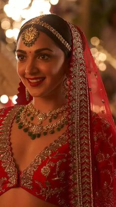 a woman wearing a red and gold bridal outfit with jewels on her head, smiling