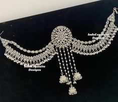 an elaborate necklace is displayed on a black surface with white beads and chains hanging from it