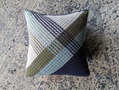 a blue and green pillow sitting on top of a gray floor next to a wall