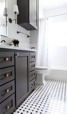 a bathroom with black and white tile flooring and cabinets, along with a toilet