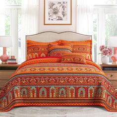 a bed with an orange and red bedspread in front of two lamps on a table