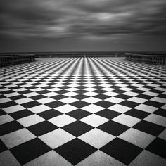 an abstract black and white checkered floor with dark clouds in the sky above it