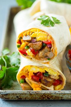 two burritos on a tray with salsa and cilantro in the background