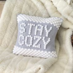 a knitted pillow that says stay cozy on top of a fluffy white fur blanket