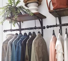 a bunch of clothes hanging on a rack next to a potted plant