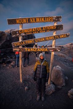 a person standing in front of a sign on top of a mountain