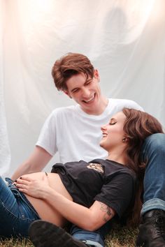 a man and woman laying on the ground together smiling at each other with their arms around one another