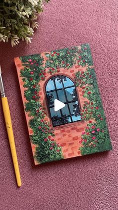 an open book with a window on it next to a brush and flower pot filled with flowers