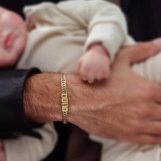 a close up of a person holding a baby with a gold bracelet on it's wrist